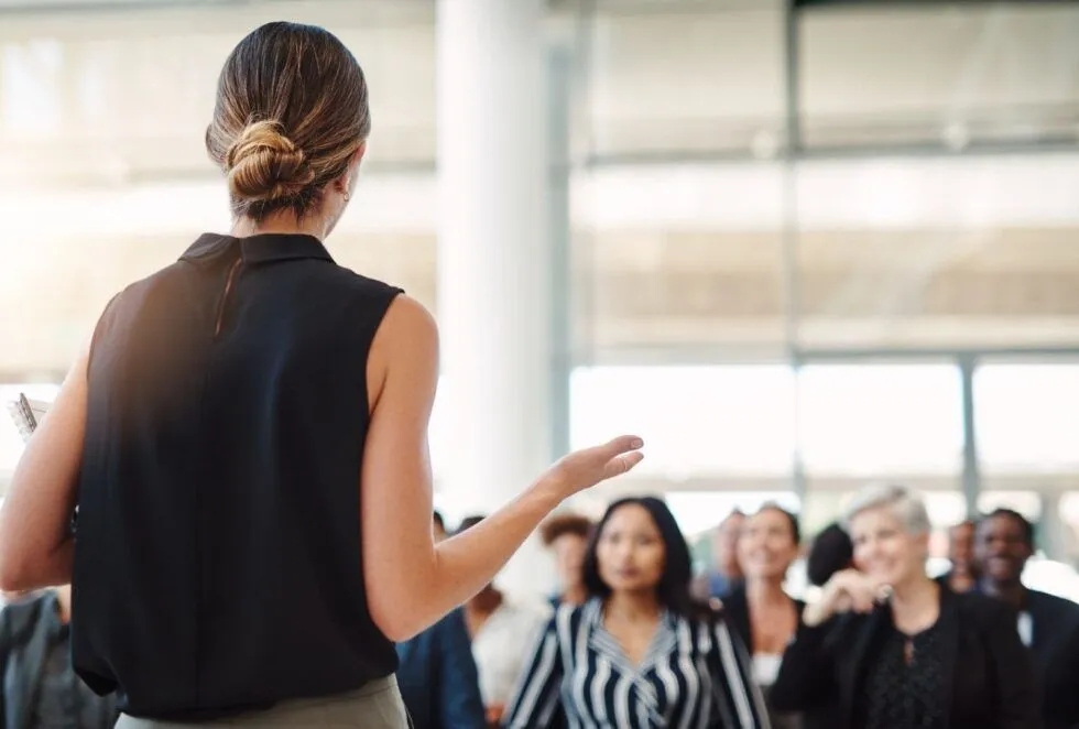 A woman speaks in front of a seated group