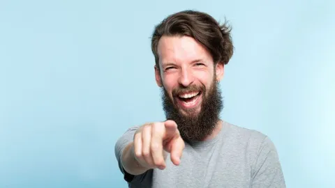 A bearded man laughs and points at the camera