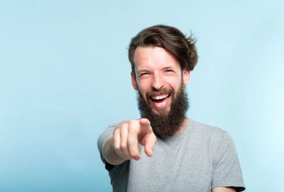 A bearded man laughs and points at the camera