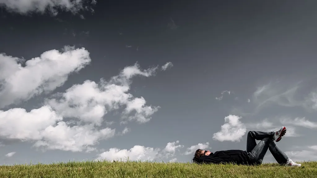 Une personne allongée dans l’herbe regarde les nuages