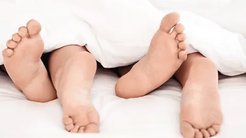 Zwei Personen liegen unter einer Decke, ihre Füße sind sichtbar