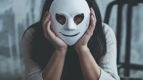 A young woman holds a white mask in front of her face