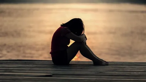 A person sits alone by the water at dusk