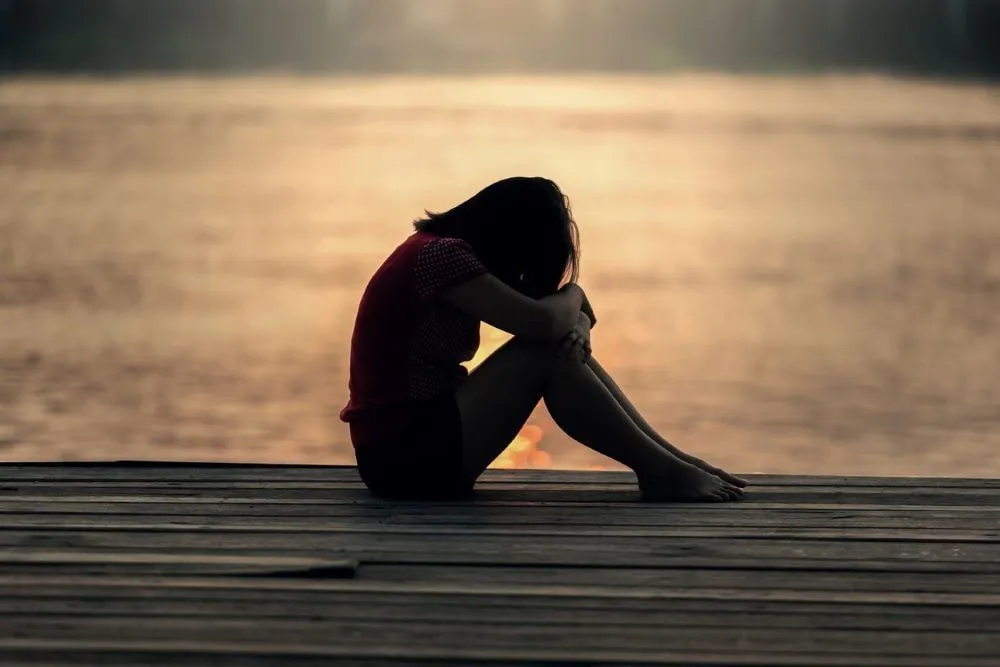 A person sits alone by the water at dusk