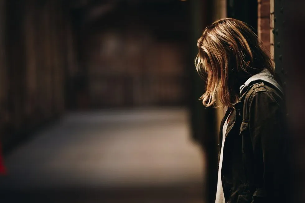 A woman alone with her head bowed in a dark room