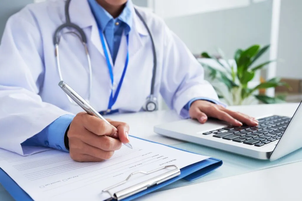 Médecin remplissant un dossier à côté d’un ordinateur portable