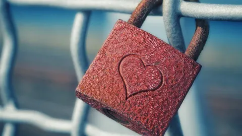 Candado rojo con un corazón sujeto a una reja