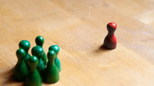 Eine einzelne rote Figur steht einer Gruppe grüner Figuren gegenüber