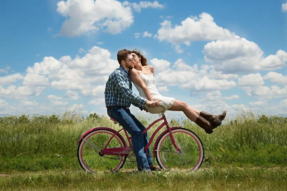 A couple kisses on a bicycle in a field