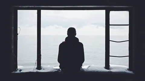 Silhouette einer Person allein vor einem großen Fenster